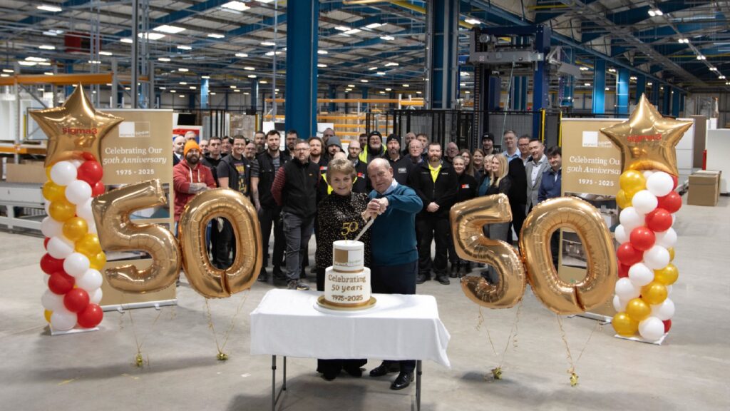 Man and wife cutting a cake in a factory with balloons in the shape of number 50